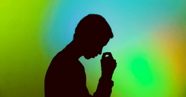 Silhouette of a stressed man sitting with his head in his hands against a green and blue gradient background.