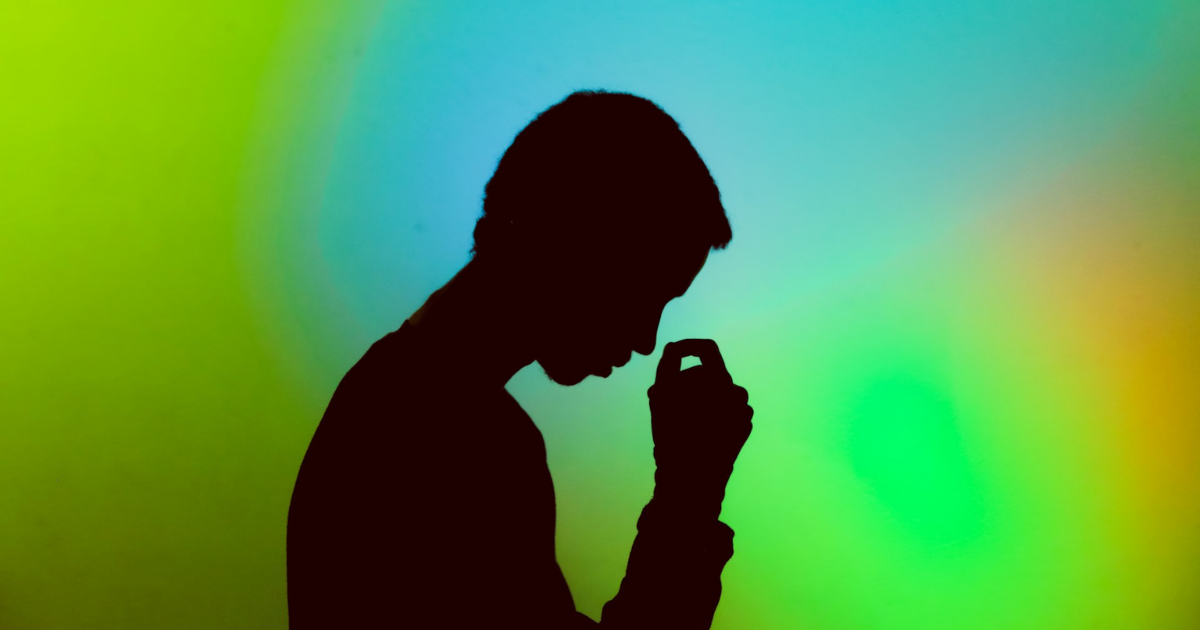 Silhouette of a stressed man sitting with his head in his hands against a green and blue gradient background.