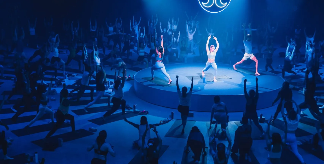 A circle of people performing yoga around a stage with instructors in the middle at a yoga brand activation event.